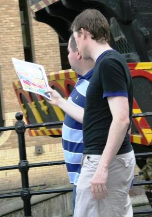 Two men study a treasure hunt clue by the replica of the Golden Hinde.