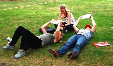 Three girls lying on the grass reading a treasure hunt clue.