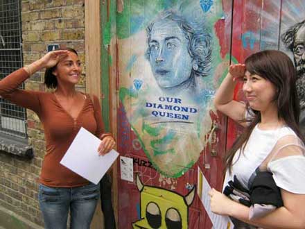 Two girls salute an image of Queen Elizabeth 11 as part of their London team building pose challenge.