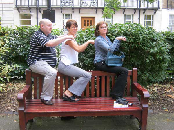 Three people sitting on a bench as one of their poses.