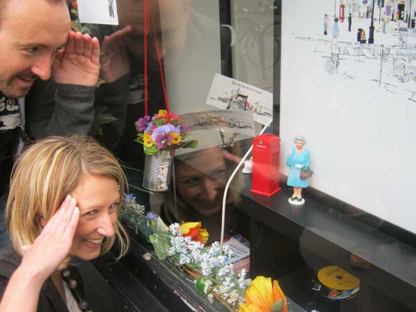 A man and a woman saluting a miniature queen in a shop window.