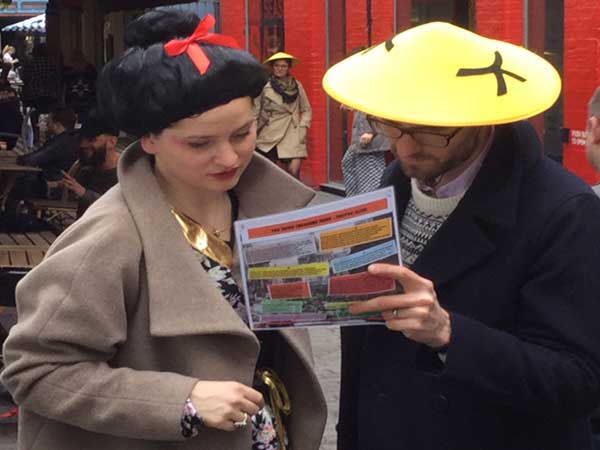 A man and a woman wearing chinese hats read a clue on their Soho quest in Chinatown.