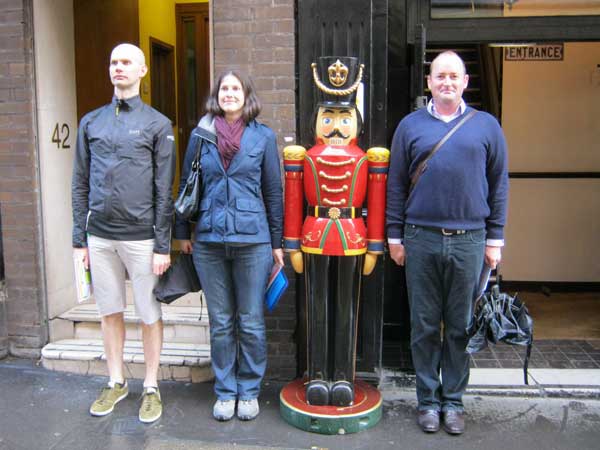 Three people posing alongside a toy soldier.